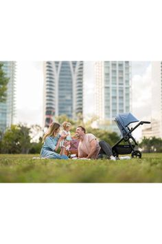 a family sitting on the grass with their baby in a stroller next to them