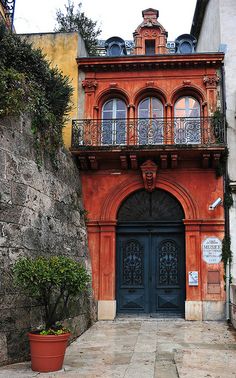 an old building with a blue door and balcony on the top floor next to a stone wall