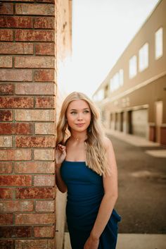 a woman in a blue dress leaning against a brick wall