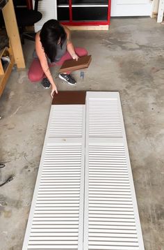 a woman kneeling on the ground next to a floor mat with two pieces of wood in front of her