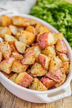 a white casserole dish filled with cooked potatoes and parsley on the side