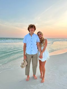 a man and woman holding hands on the beach at sunset with waves in the background