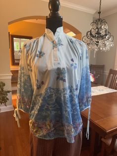 A vintage semi sheer blouse in blue.  This unique blouse has a stand up collar and 3 buttons at the neckline.  Light blue with random flower and leaves at the top of the blouse, which become more prominent at the bottom.  3/4 sleeves with ties.  In good vintage condition with no rips or stains.  Shown on a size 6 dress form with a 34 inch bust and 26 inch waist.  The bust of the blouse measures 18 inches from armpit to armpit laying flat, 24 inches from shoulder to hem and 13.5 inches from shoul Vintage Blouses, Flower And Leaves, Light Blue Flowers, Unique Blouse, Flower Leaf, Dress Form, Size 6 Dress, Print Blouse, Leaf Print