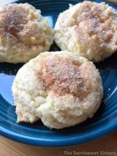 three biscuits on a blue plate with sugar sprinkled on top, sitting on a wooden table