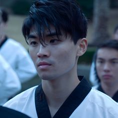 a young man with black hair wearing a white and black shirt looking at the camera