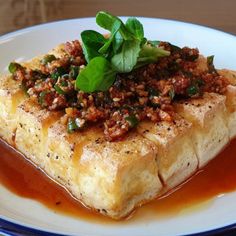 a white plate topped with meat covered in sauce and garnished with green leaves