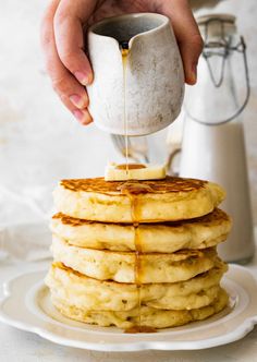 a stack of pancakes being drizzled with syrup by a person pouring syrup on them