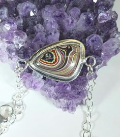 a piece of jewelry sitting on top of a pile of purple rocks next to a chain