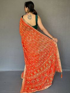 Look stunning in this classic orange printed georgette festival wear saree with a blouse! The saree is 5.50 meters long and made of high-quality georgette material with bandhani print all over, and gotta pati lace border with tassels work. The green blouse in georgette material with a gotta patti lace border adds a beautiful contrast to the saree. The saree is perfect for weddings, festivals, events, or even casual wear. It's customizable and comes with an stitched 1.00 meters blouse. Orange Georgette Sharara For Navratri, Traditional Orange Art Silk Pre-draped Saree, Orange Georgette Sharara With Traditional Drape, Orange Traditional Wear For Festive Transitional Season, Orange Georgette Sharara With Zari Work, Orange Georgette Sharara For Festivals, Traditional Orange Pre-draped Saree For Festive Occasions, Orange Pre-draped Designer Saree For Festive Occasions, Festive Designer Orange Pre-draped Saree