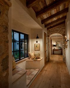 a long hallway with stone walls and wooden flooring is lit by lights from the windows