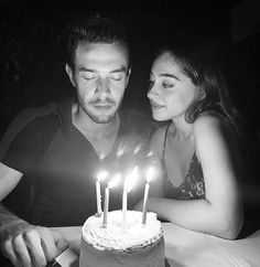 a man and woman sitting in front of a cake with lit candles on top of it