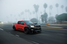 a red truck driving down the road with palm trees in the background on a foggy day