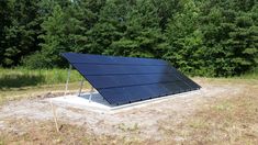 a solar panel sits in the middle of a field with trees in the back ground