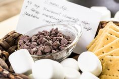 marshmallows and crackers are in a bowl next to a note on a table