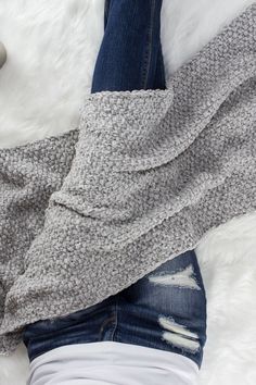 a woman laying on top of a white rug wearing ripped jeans and a gray sweater