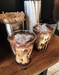 three glasses filled with ice cream sitting on top of a wooden table next to drinks