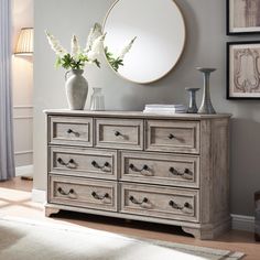 a white vase with flowers sitting on top of a wooden dresser next to a mirror