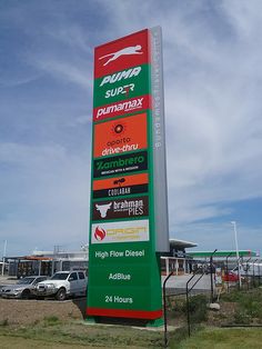 a large sign in front of a parking lot with cars parked behind it and the sky above