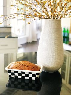 a white vase filled with yellow flowers next to a loaf of bread on a table