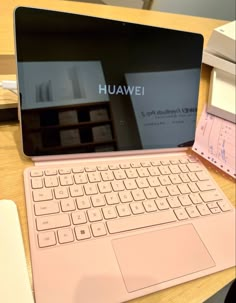 an open laptop computer sitting on top of a wooden table next to a pink keyboard