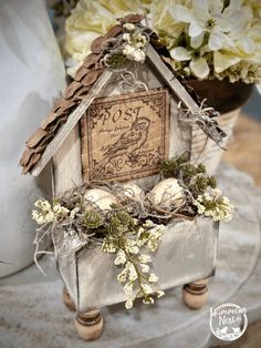 a bird house with some flowers in front of it and a postcard on the top