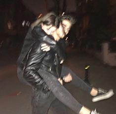 a man and woman are hugging on the street at night, one is holding the other's leg