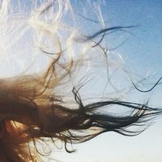 a woman with her hair blowing in the wind on a sunny day at the beach