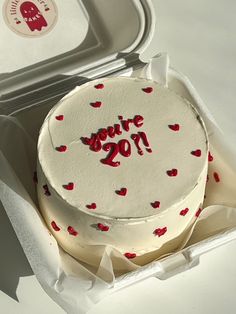 a white cake with red hearts on it in a box next to a container that says i love you