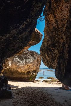 a person is standing on the beach between two large rocks