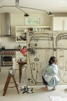 a woman standing in front of a drawing on the wall next to a stove top oven