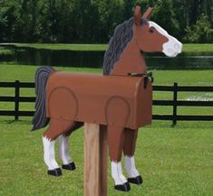 a cardboard horse standing on top of a lush green field next to a wooden fence