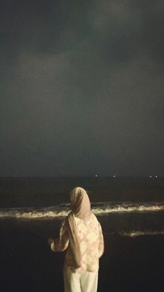 a woman standing on top of a beach next to the ocean under a cloudy sky