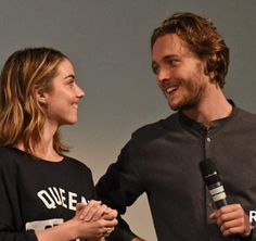 a man and woman standing next to each other holding microphones in their hands while smiling