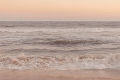 an ocean view with waves crashing on the shore and pink sky in the back ground