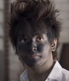 a man with black face paint on his face and hair in front of brick wall