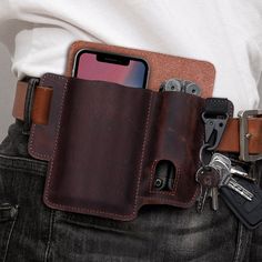 a man is holding his cell phone and some keys in his back pocket while wearing a leather belt