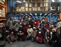 a group of people wearing masks posing for a photo in a warehouse with boxes on the floor