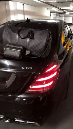 the back end of a black car with luggage on it's trunk in a parking garage