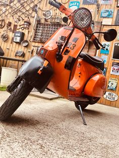 an orange scooter parked in front of a wooden wall with clocks on it