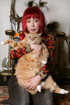 a woman with red hair is holding a cat in her arms and posing for the camera