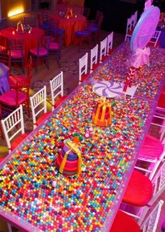 a long table covered in lots of colorful candies next to white chairs and tables