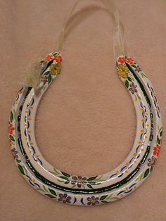 three white and multicolored flowers decorated ceramic necklaces on a beige surface with a feather