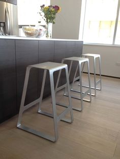 three metal stools sitting in front of a counter top next to a vase with flowers