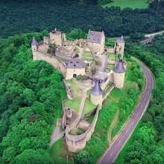 an aerial view of a castle in the middle of green trees and grass with a road running through it