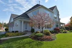 a white house with trees and bushes in front of it on a nice sunny day