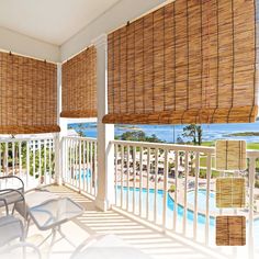 a balcony with wicker shades and chairs overlooking the pool