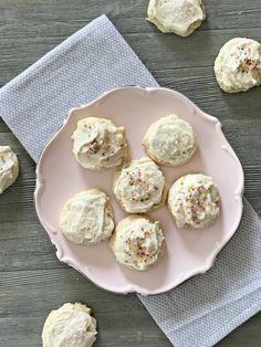 white frosted cookies with sprinkles on a pink plate next to a napkin