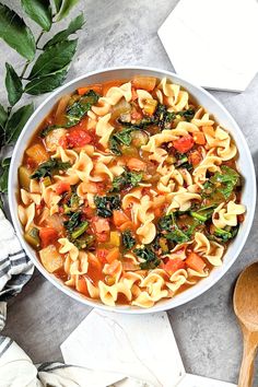 a bowl filled with pasta and vegetables next to a wooden spoon on top of a table