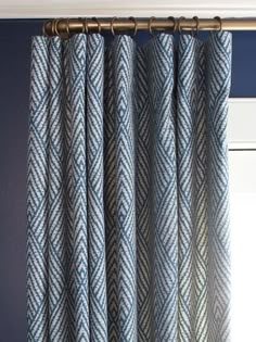 a blue and white patterned curtain hanging on a metal rod in front of a window