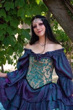 a woman in a blue dress is sitting under a tree with her hands on her hips